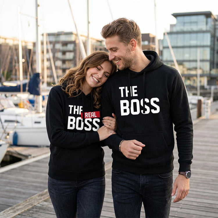 Paar in schwarzen Partner Hoodies mit „The Boss“ und „The Real Boss“ Motiv am Yachthafen