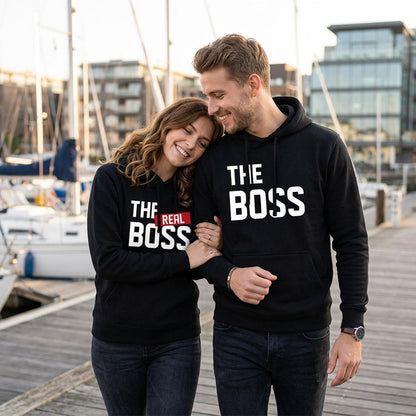 Paar in schwarzen Partner Hoodies mit „The Boss“ und „The Real Boss“ Motiv am Yachthafen